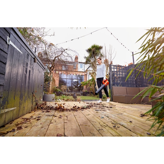 Photo of BLACKDECKER BCBL200B leaf blower in use clearing leaves on a wooden patio in a garden setting.