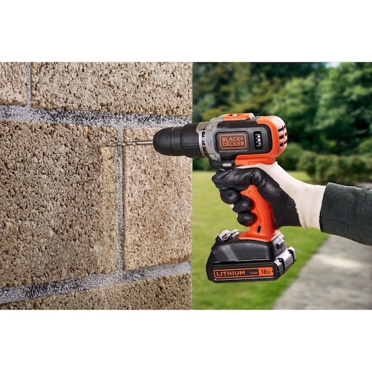 BLACKDECKER cordless drill BCD003C1 used to drill into a stone wall, close-up, outdoor setting.