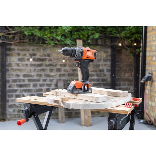 BLACK+DECKER cordless drill on a workbench with wooden boards, outdoors with brick wall background.