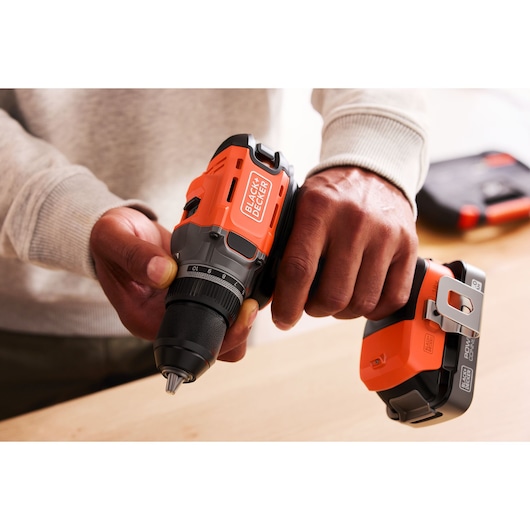 Person holding a BLACK+DECKER cordless power drill with orange and black details on a wooden surface.