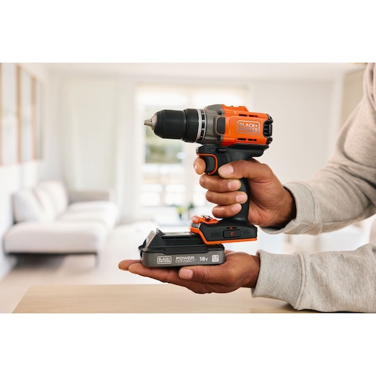 Photo of BLACK+DECKER 18V cordless drill driver BCD382D1, held in hand inside a modern living room.