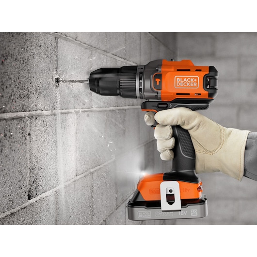 Hand drilling concrete wall with BLACK+DECKER cordless drill, orange and black, 18V battery.