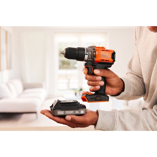 BLACK+DECKER BCD383D1 cordless drill with orange and black design and 18V battery, held indoors.