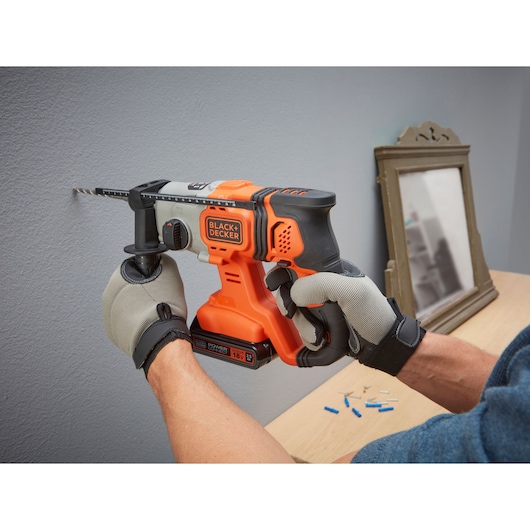 Photo of BLACK+DECKER BCD900E2K cordless hammer drill in use on a wall, orange and black design, gloved hands.