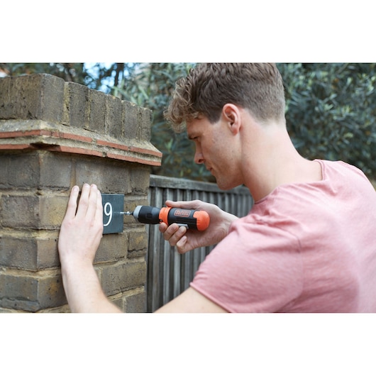 BLACKDECKER BCF601C cordless screwdriver used to mount a house number on a brick wall outdoors.