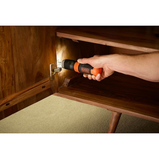 BLACKDECKER BCF601C cordless screwdriver used on a cabinet hinge inside a wooden cupboard.