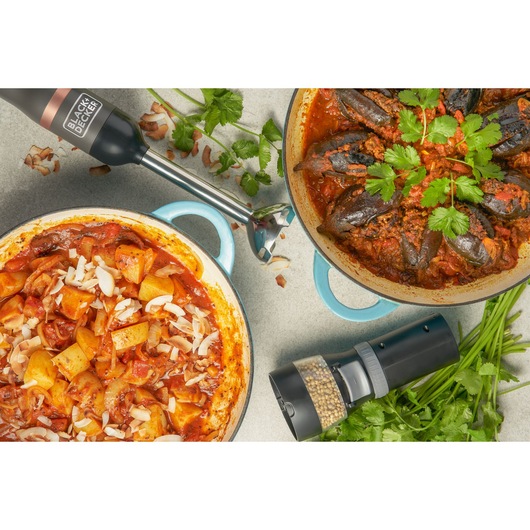 Photo of BLACK+DECKER BCKM1016KSG hand blender and grinder with two pots of cooked food and herbs on a kitchen counter.