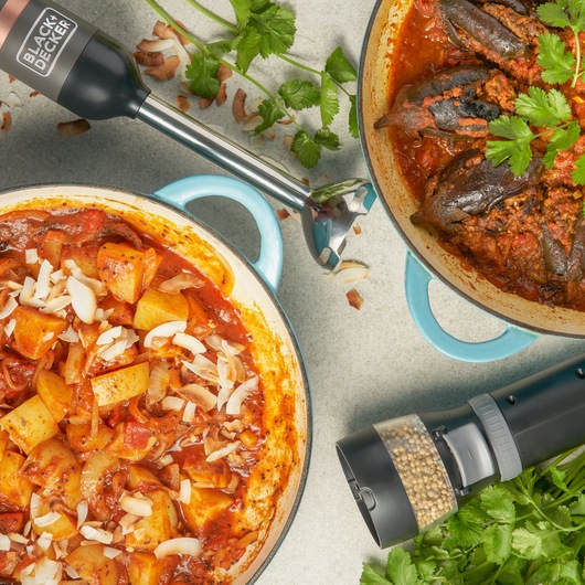 BLACK+DECKER BCKM1016KSG hand blender and grinder with fresh herbs beside two blue pots containing curry dishes, top view.