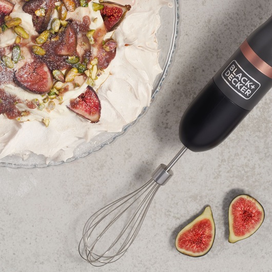 BLACK+DECKER BCKM101WHFF hand mixer with whisk attachment, next to a dessert topped with figs and pistachios.