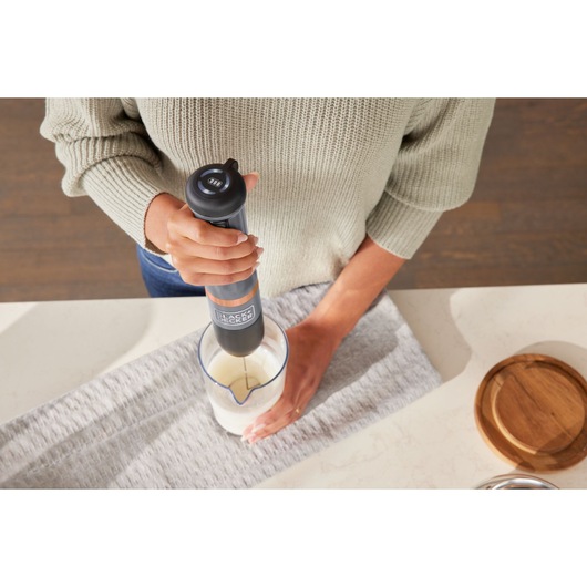 BLACKDECKER hand blender BCKM1012KG in use blending ingredients in a clear measuring cup on a kitchen counter.