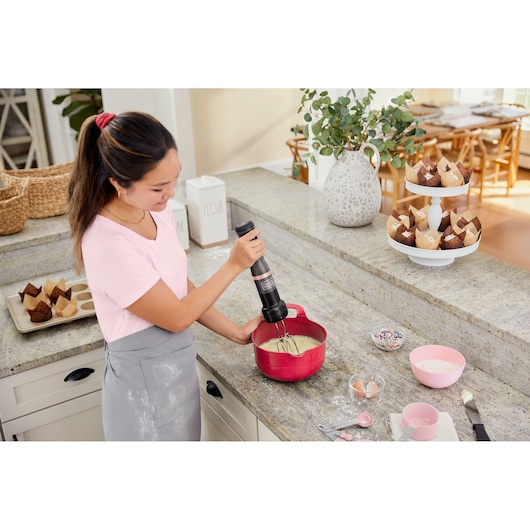 BLACK+DECKER BCKM101HM hand mixer used to blend batter in red mixing bowl on kitchen counter.