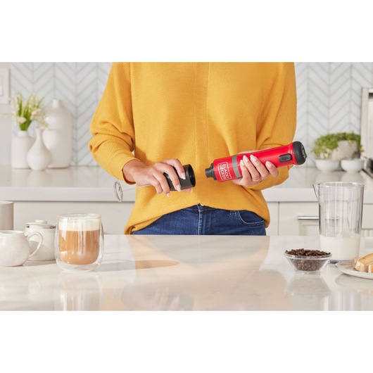 Photo of BLACKDECKER BCKM101MFFF red handheld milk frother in use in a modern kitchen setting.