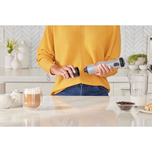 Photo of BLACKDECKER BCKM101MFFF handheld milk frother in use on kitchen counter with latte and coffee beans.