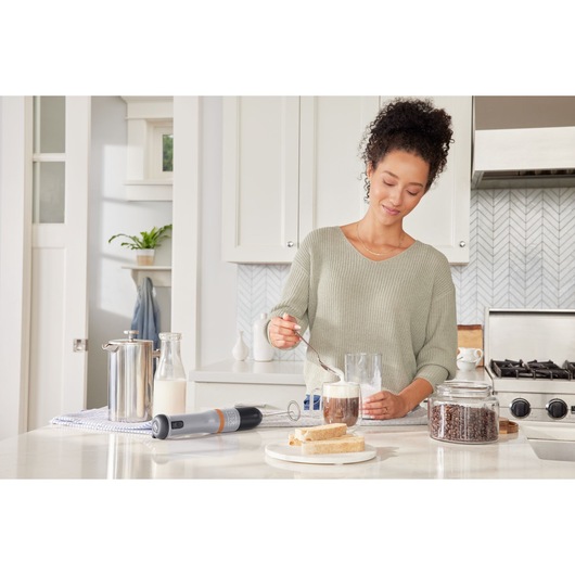 BLACKDECKER BCKM101MFFF handheld milk frother on kitchen counter near coffee, milk, bread, and coffee beans.