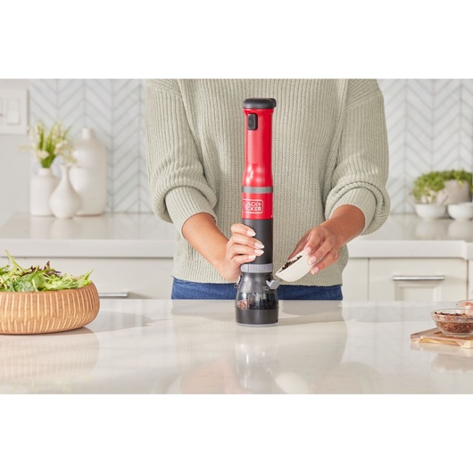 BLACK+DECKER BCKM101SPFF electric grinder in use on kitchen counter, person pouring peppercorns.