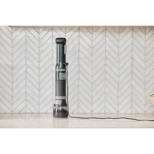 Photo of BLACKDECKER handheld vacuum cleaner BCKM101SPFF charging on a countertop with white tile background.