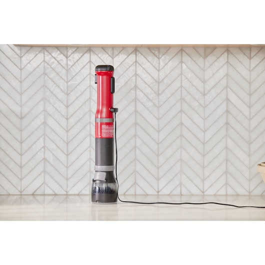 Photo of BLACKDECKER BCKM101SPFF red and black stick vacuum standing upright on kitchen counter with cord extended.