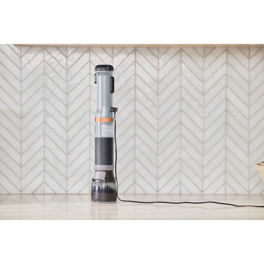 BLACKDECKER BCKM101SPFF stick vacuum cleaner upright on kitchen counter, gray and orange, front angle.