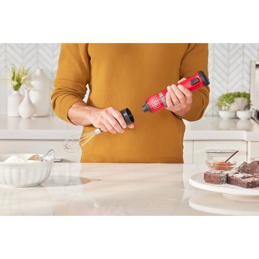 BLACKDECKER BCKM101WHFF cordless hand mixer in red held over kitchen counter with baking ingredients.