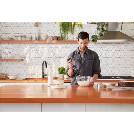 BLACKDECKER BCKM101WHFF hand mixer used in a modern kitchen with wooden countertop and baking ingredients.