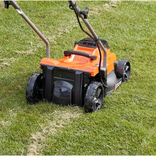 BLACK+DECKER BCMW3318L2 lawn mower rear view on green grass, showing large wheels and orange body.