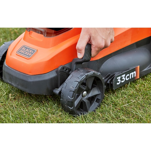 Close-up photo of BLACK+DECKER BCMW3318L2 lawn mower wheel and handle, showing 33cm cutting width, used on grass.