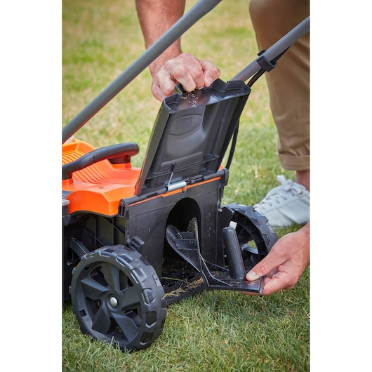 BLACK+DECKER BCMW3318L2 lawn mower close-up showing open rear flap and wheels on grass.