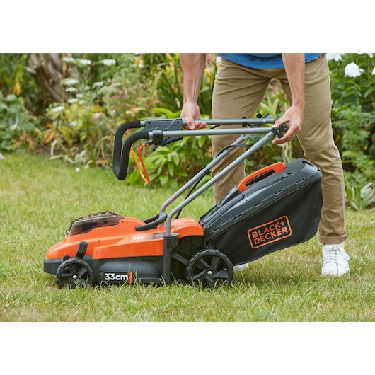 BLACK+DECKER BCMW3336L1 cordless lawn mower with black and orange design, folding handle, grass collection bag, outdoor use.