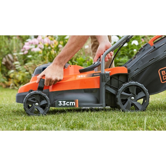 Photo of BLACKDECKER BCMW3336L1 cordless lawn mower side view, 33cm cutting width, person adjusting height.