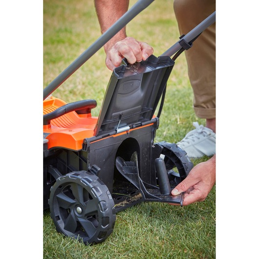 Photo of a BLACK+DECKER BCMW3336L1 lawn mower, close-up of a person opening the rear flap and compartment.