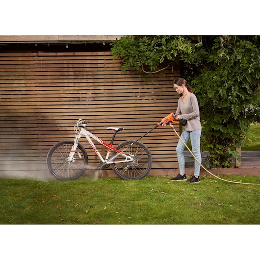 BLACKDECKER BCPC18B pressure washer cleaning a bicycle outdoors on grass near wooden fence.