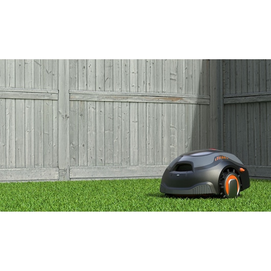 BLACKDECKER BCRMW122 robotic lawn mower on grass near a wooden fence, side angle.
