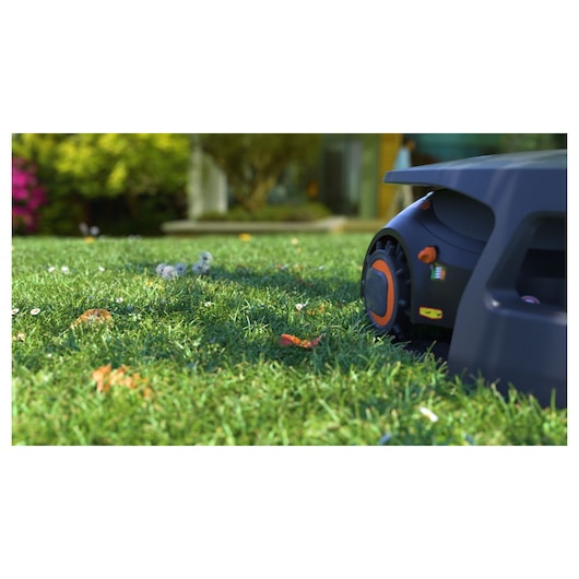 BLACKDECKER BCRMW123 robotic lawn mower on grass, close-up outdoor angle, dark body with orange accents.
