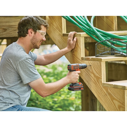 BLACKDECKER BDCDC18 cordless drill used outdoors on wooden stairs, visible orange and black design.