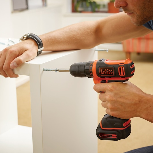 BLACKDECKER BDCDD121 cordless drill being used to assemble white furniture.