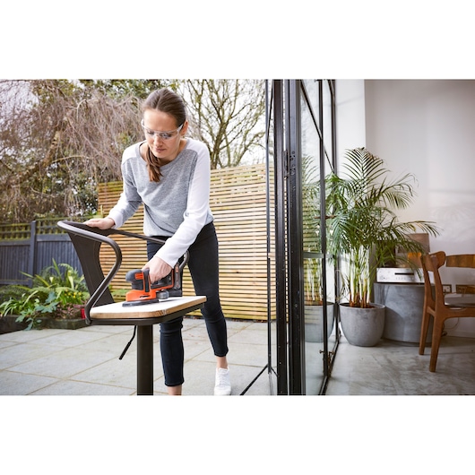 Photo of BLACKDECKER BDCDS18 sander used to sand a chair outdoors next to a patio door.