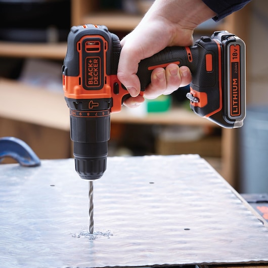 BLACK+DECKER BDCHD18K1B2 cordless drill in use, drilling into a metal sheet, close-up side angle.