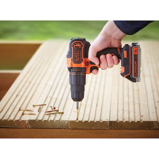 BLACKDECKER BDCHD18KB2 cordless drill, orange-black, being used to drive screws into wooden planks.
