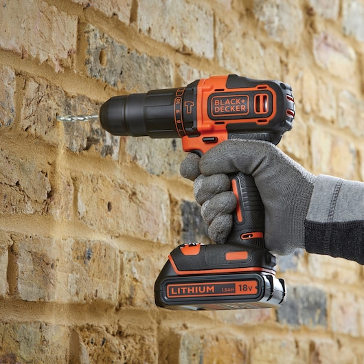 Photo of BLACK+DECKER BDCHD18KB cordless drill being used to drill into a brick wall, shown in a gloved hand.
