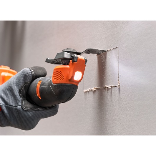 BLACKDECKER BDCOS18D1K oscillating multi-tool cutting drywall, close-up with gloved hand and LED light.