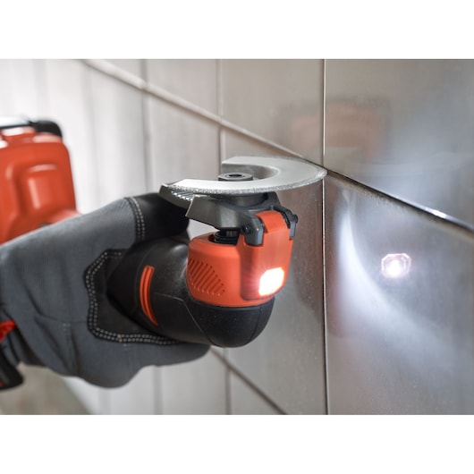 BLACKDECKER BDCOS18N oscillating multi-tool in use cutting tile grout, close-up angle, LED light on.