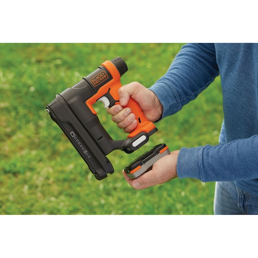 BLACKDECKER BDCT12N cordless nail gun with battery being detached, held outdoors.