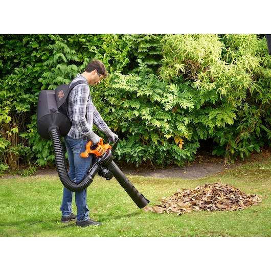 BLACKDECKER BEBLV290 garden vacuum and blower in use collecting leaves, outdoor setting with green foliage.