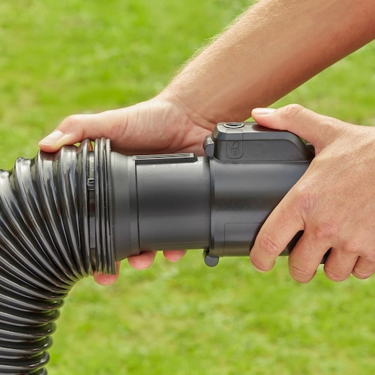 Close-up of BLACK+DECKER BEBLV300 leaf blower flexible hose connection held by hands outdoors.