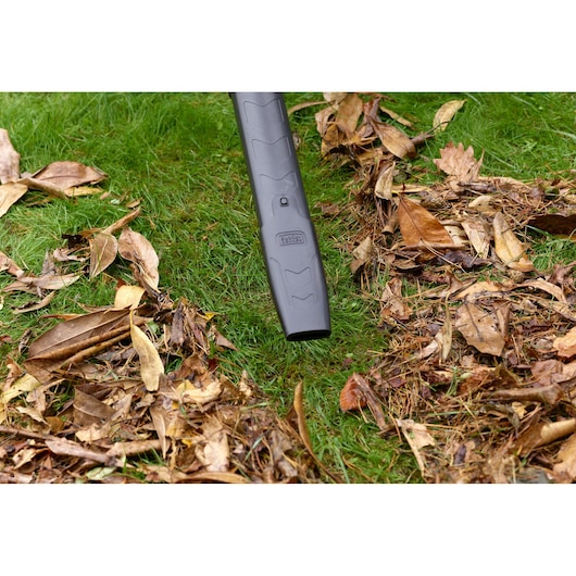 BLACKDECKER BEBLV301 leaf blower nozzle clearing dry leaves on lawn, close-up outdoor photography.