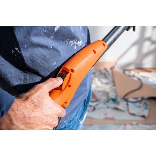 Hand holding an orange BLACK+DECKER power tool with trigger, close-up during home renovation.