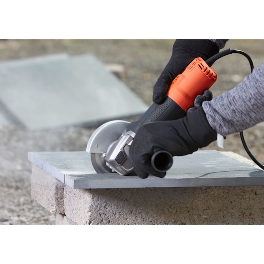 BLACKDECKER BEG210K angle grinder cutting stone slab, close-up with gloved hands, outdoor setting.