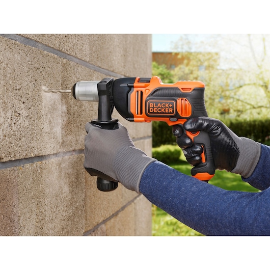 BLACK+DECKER BEH850K hammer drill in use drilling into a concrete wall outdoors.