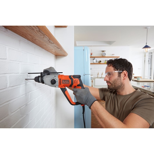 BLACKDECKER BEHS02K corded hammer drill used on white brick wall in a kitchen setting.