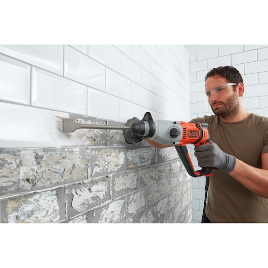 BLACKDECKER BEHS02K hammer drill removing tile from wall, side view, orange and gray tool.